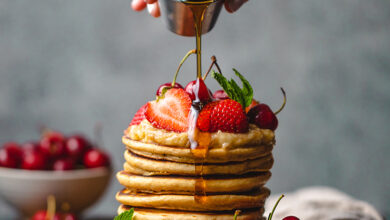 Photo of a stack of pancakes and a hand pouring syrup on them
