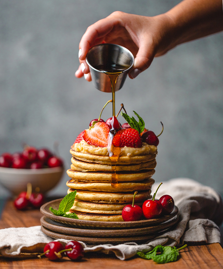 Photo of a stack of pancakes and a hand pouring syrup on them