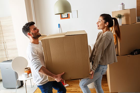 Young couple carrying big cardboard box at new home.