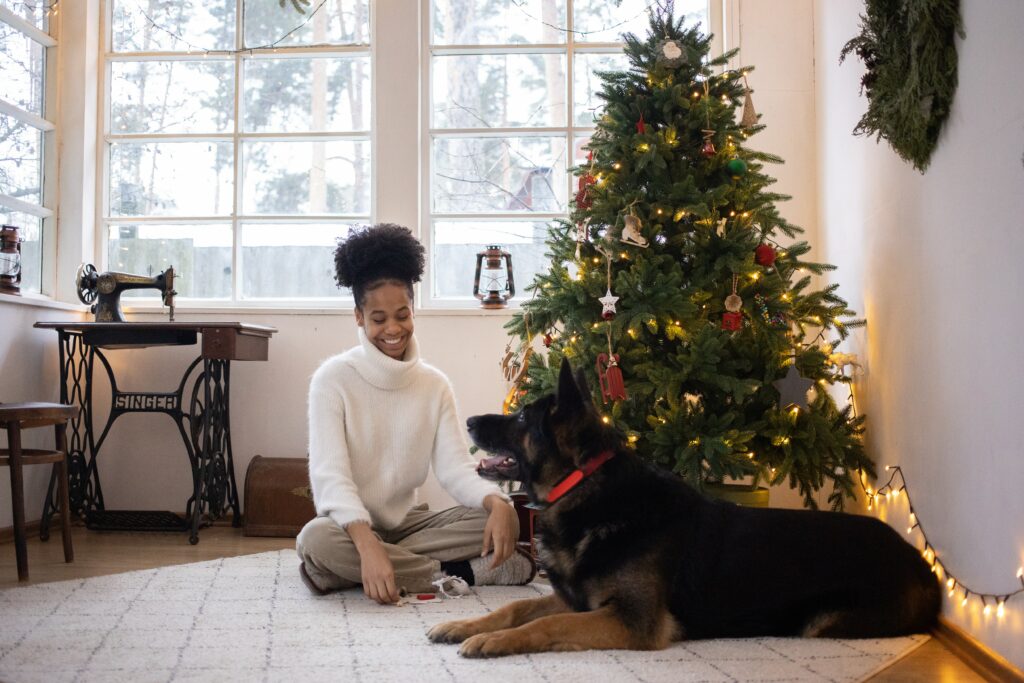 Woman sat by her lit-up Christmas tree with her dog. 