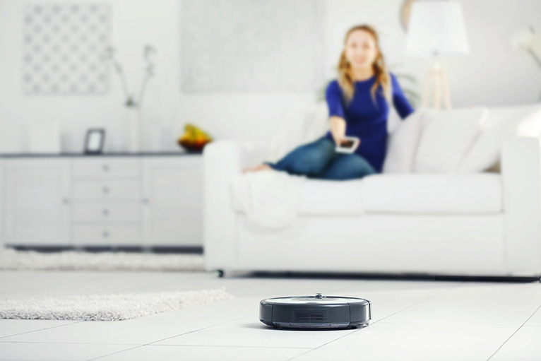 Girl on sofa operating a robot vacuum cleaner