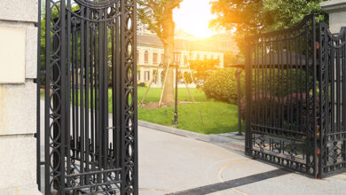 Large iron gates open to show a mansion within in the sun