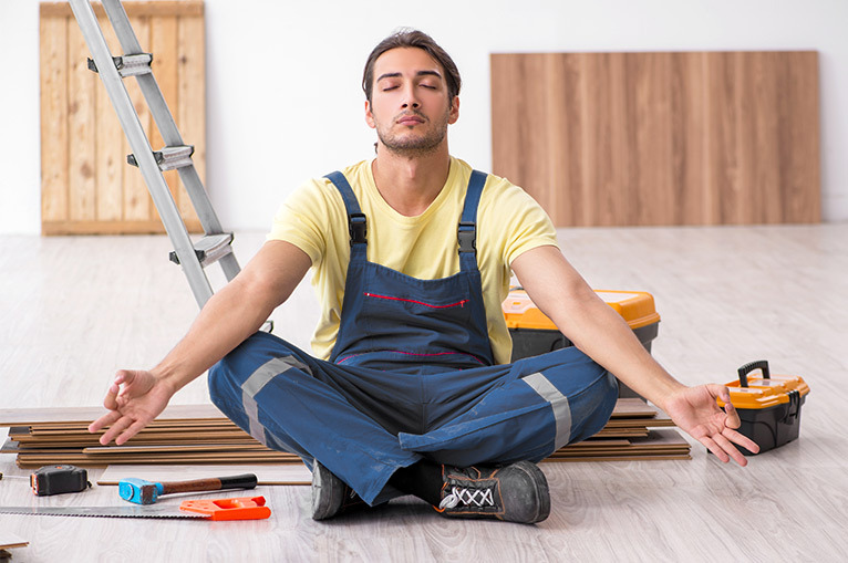 Tradesperson sitting down to meditate with tools and equipment in the background