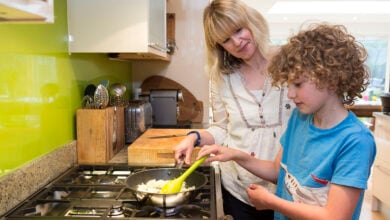 Mother helping her young son to cook on a gas hob