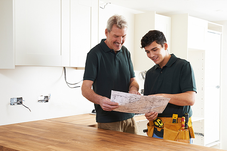 Electrician and apprentice smiling at site plans