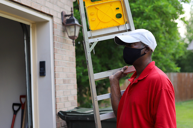 Tradesperson wearing a mask and carrying a ladder into a customer's home