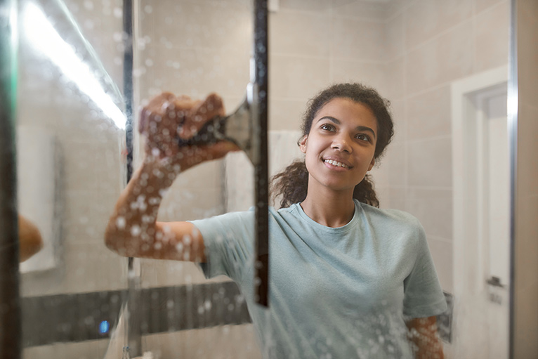 Smiling woman using a squeegee to clean her shower