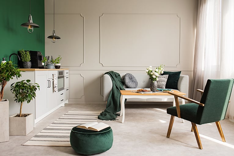 Open plan kitchen with green design accents, including a pouffe, blanket and cushions