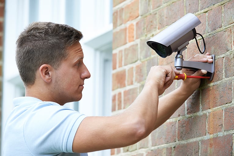 Security specialist installing a home security camera on the outside of a house