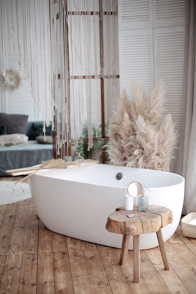 Freestanding bath in rustic bathroom with wood floorboards and pampas grass