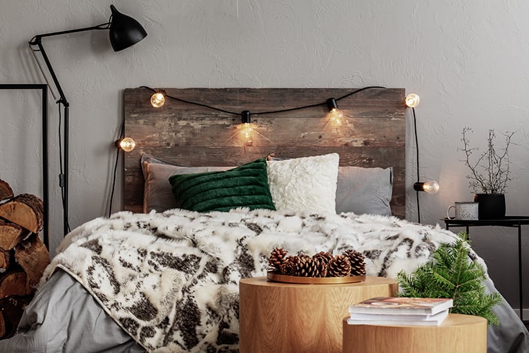 Bed with rustic wooden headboard, fairylights, lamp and cosy blankets