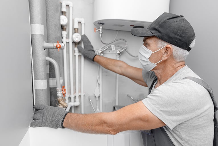 Plumber wearing mask in home, looking at pipes