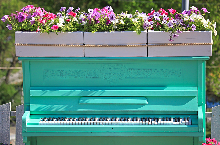 Teal piano with flower planters on top in garden