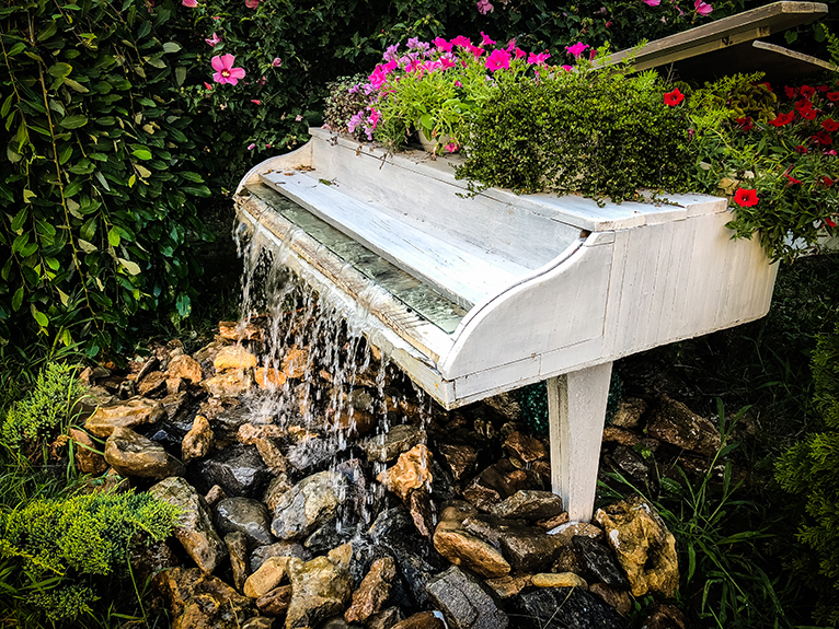 Hollowed out grand piano in garden with plants and water feature