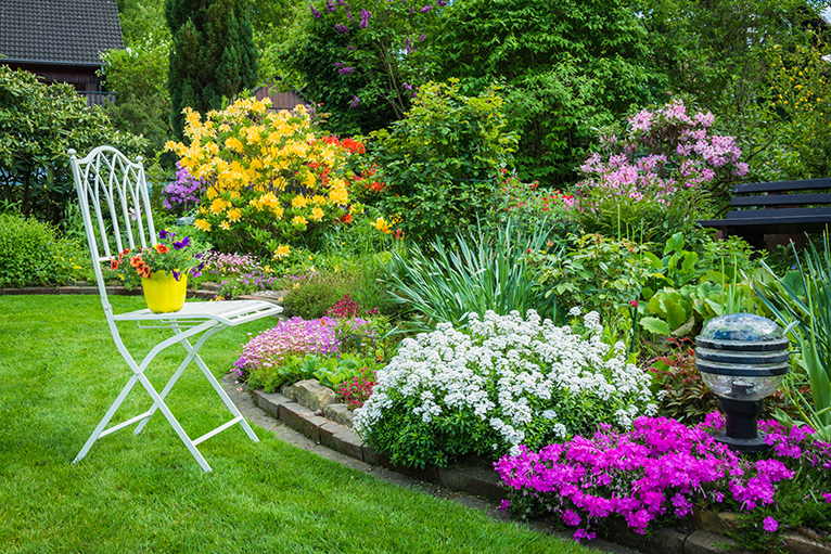 Garden with blooming flowerbeds and decorative garden chair
