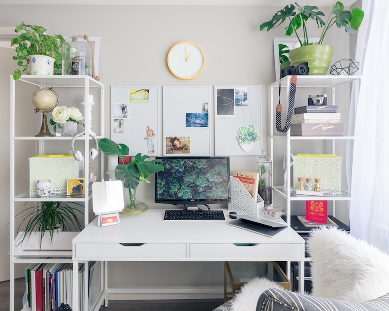 White desk decorated with surrounding plants, artwork and ornaments