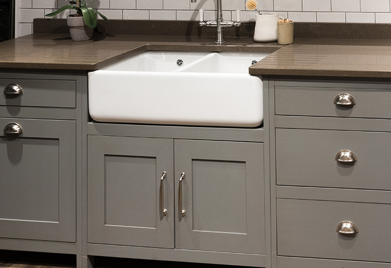 Kitchen makeover hacks: White farmhouse surrounded by grey cabinets with silver handles