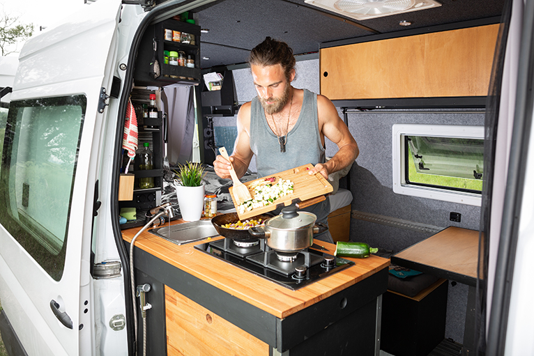 Person using spice rack storage whilst cooking in camper van