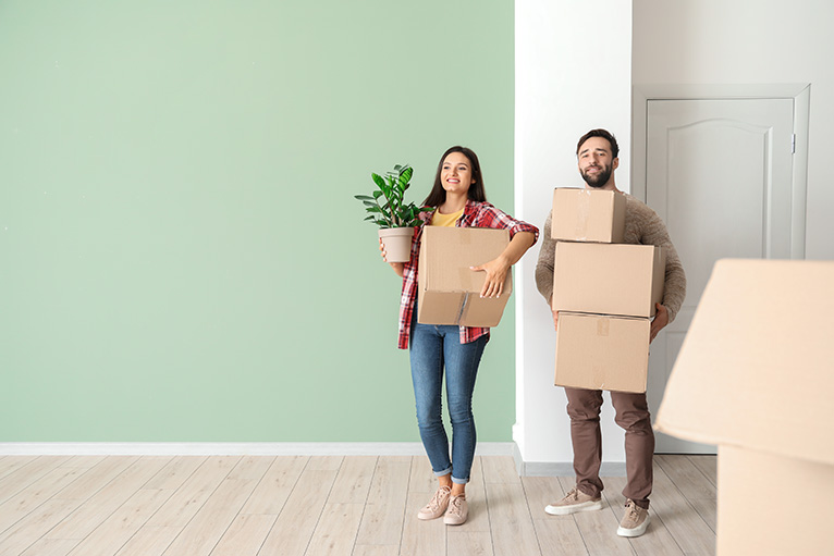 Couple carrying moving boxes into new home