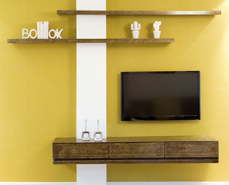 Yellow wall with white stripe, dark wood shelving, ornaments and a small wall mounted TV