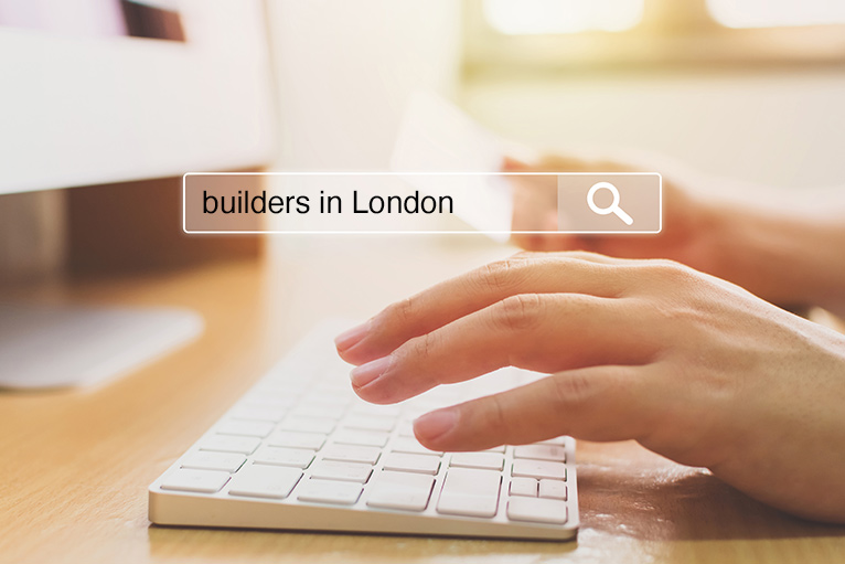 Person's hand hovering over computer keyboard - ready to search for 'builders in London'. 
