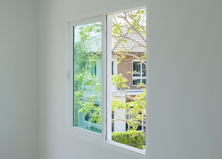 Slider window in house, looking out onto sunlit trees. 