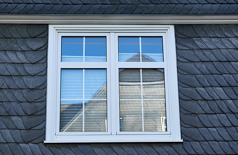 White casement window perched on the side of a house's roof. 