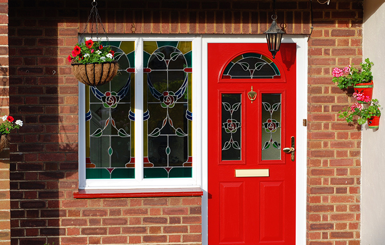 Colourful stained-glass windows with a blue and red rose design on the door and adjoining window of a house.