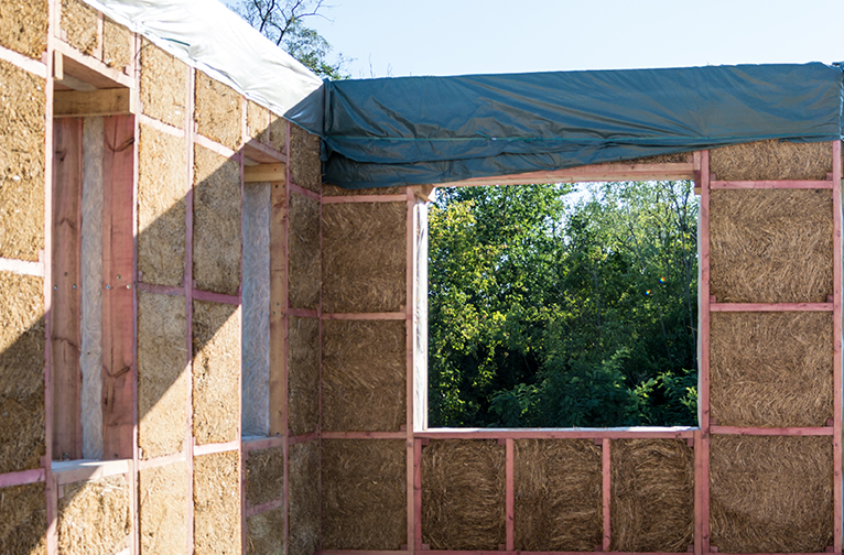 Building site showing walls of house, mid-construction, made of straw bales.