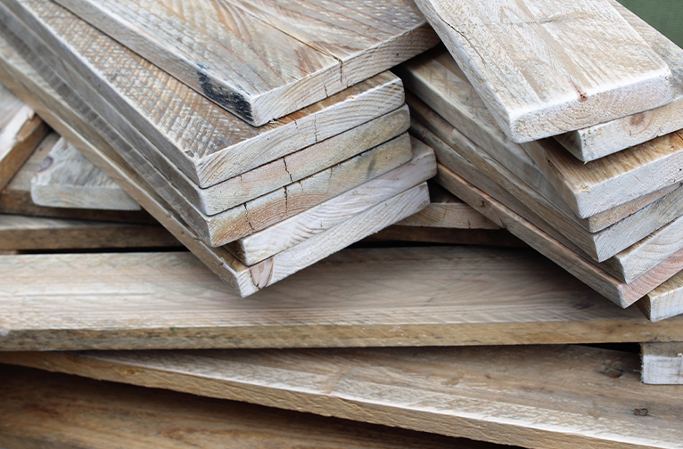 Light-coloured planks of reclaimed wood stacked in a messy pile. 