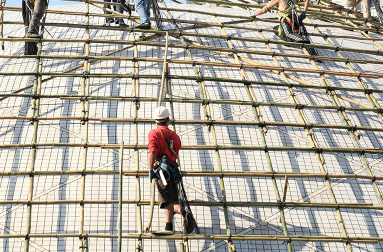 Tradesmen working on the roof of a building being constructed with bamboo. 