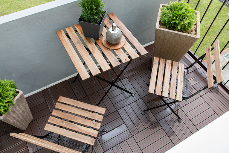 Birdseye view of wooden furniture and potted plants on a small balcony. 