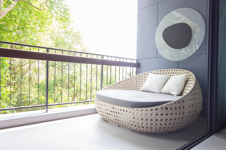 Balcony with large rattan chair-bed with eye-catching weather-resistant wall art hanging above. 