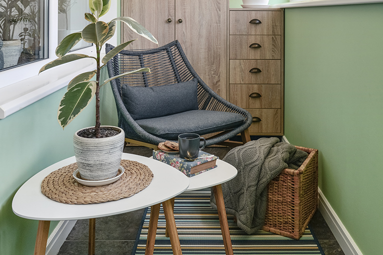 Balcony transformed into living space with a comfy rattan chair, wooden table with plant and a colourful, stripy outdoor rug. 