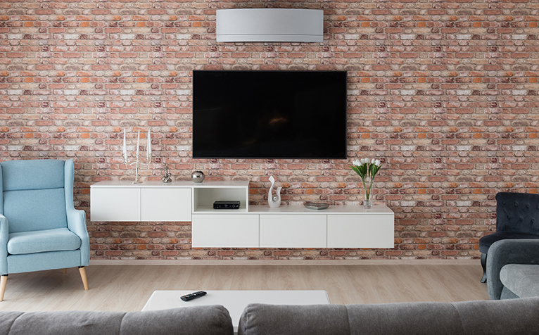 Floating home entertainment centre in living room with a large TV as a focal point hanging on a brick wall. 