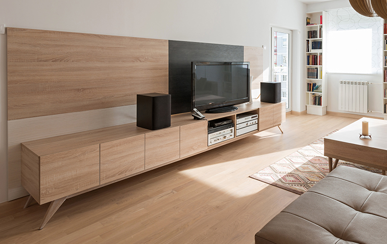 Large modern wooden block TV unit in living room with a TV and speakers sat on it. 