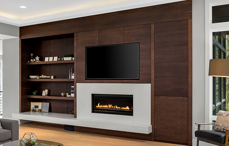 TV integrated into a wooden living room wall cabinet. An electric fire place is switched on underneath. 