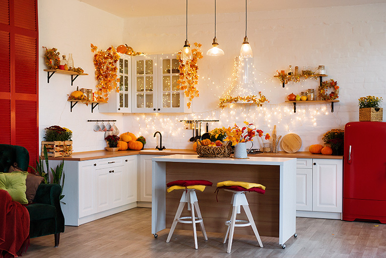 Autumn kitchen interior. Red and yellow flowers sit in a vase, and pumpkins decorate countertops. 