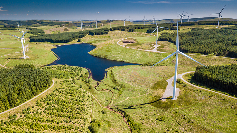 View of green fields with wind turbines spinning. 