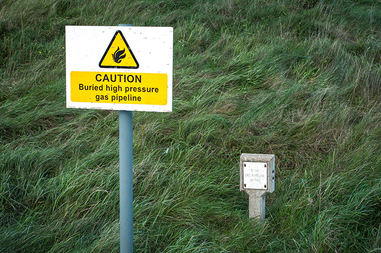 Signpost in field reading: caution buried high pressure gas pipeline.