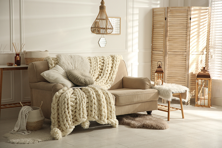 Cosy beige living room sofa dressed with a big knitted blanket and cushions.