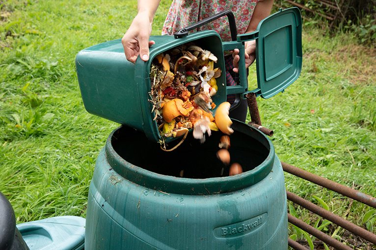 Small green compost bin filled with compost being poured into a larger green bin.