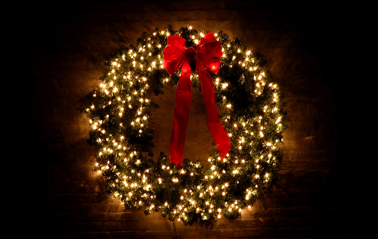 Classic Christmas wreath with lit-up fairy lights and a large red bow. 
