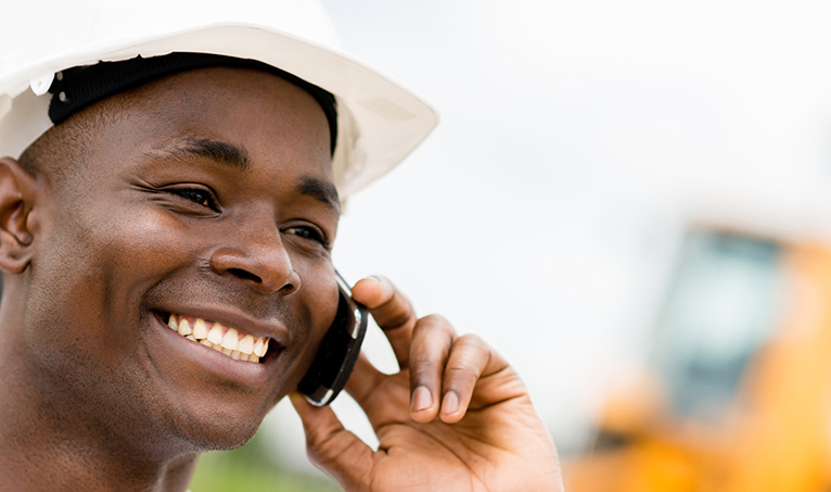 Tradesperson wearing hard-hat as he talks on the phone smiling. 