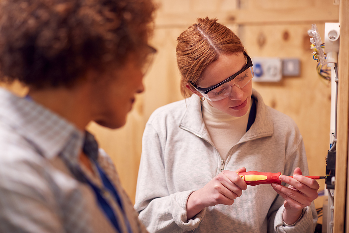 Young woman apprentice practicing fixing a plug with screwdriver while the teacher is watching