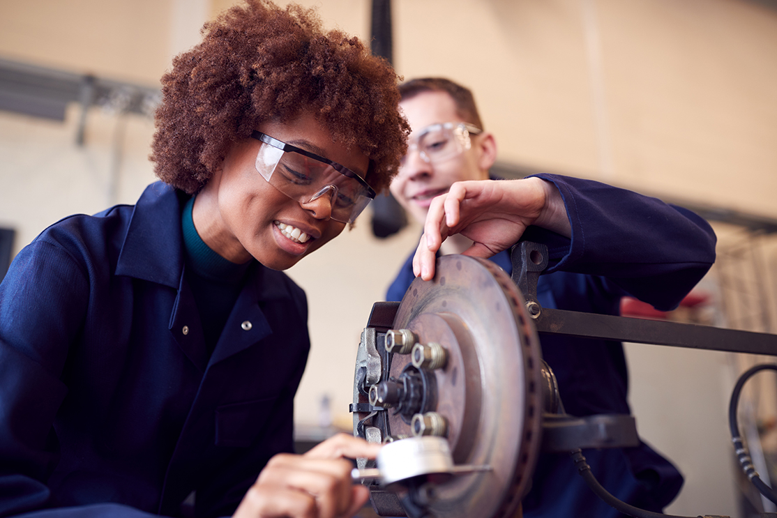 Young woman apprentice working on car brakes on auto mechanic apprenticeship course 