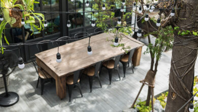 Large outdoor wooden dining table with stools and hanging lights shot from above