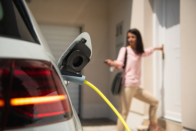 Young woman entering house next to car plugged into charging point