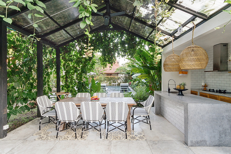 Outdoor concrete kitchen with dining table and grey chairs under a covered pergola