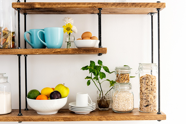 wooden open shelving wall-mounted in a kitchen, with a fruit bowl and glass jars of cereals on them.